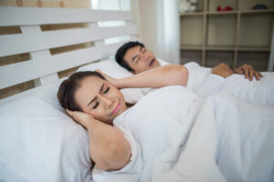 Portrait of woman blocking ears with man sleeping snoring on bed Portrait of woman blocking ears with man sleeping snoring on bed