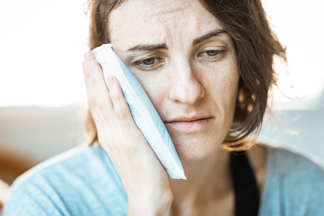 woman in blue holding side of face woman in blue holding side of face