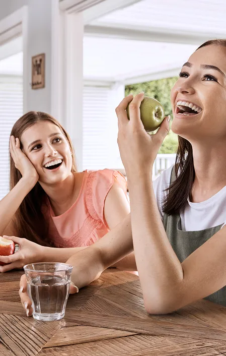 2 girls smiling and eating green apple after finishing orthodontics