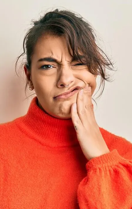 woman in pain wearing orange turtleneck holding side of face tooth pain