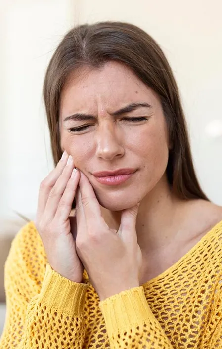 woman with yellow blouse holding side of face with toothache