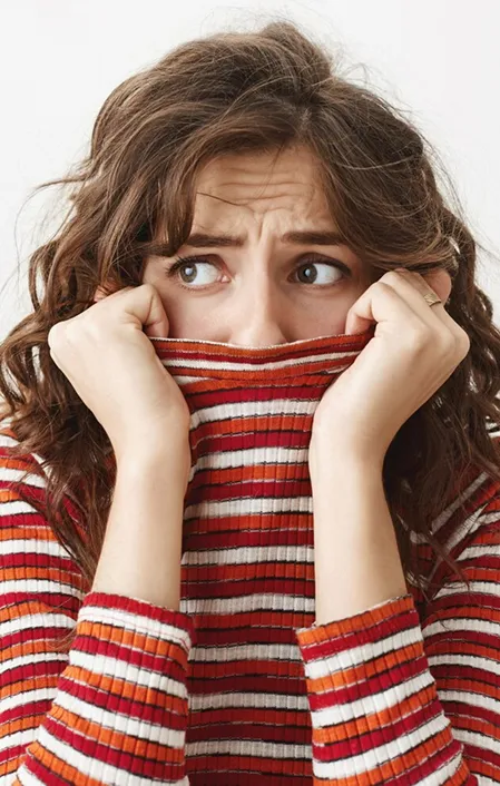 Worried woman with dental anxiety holding jumper over mouth